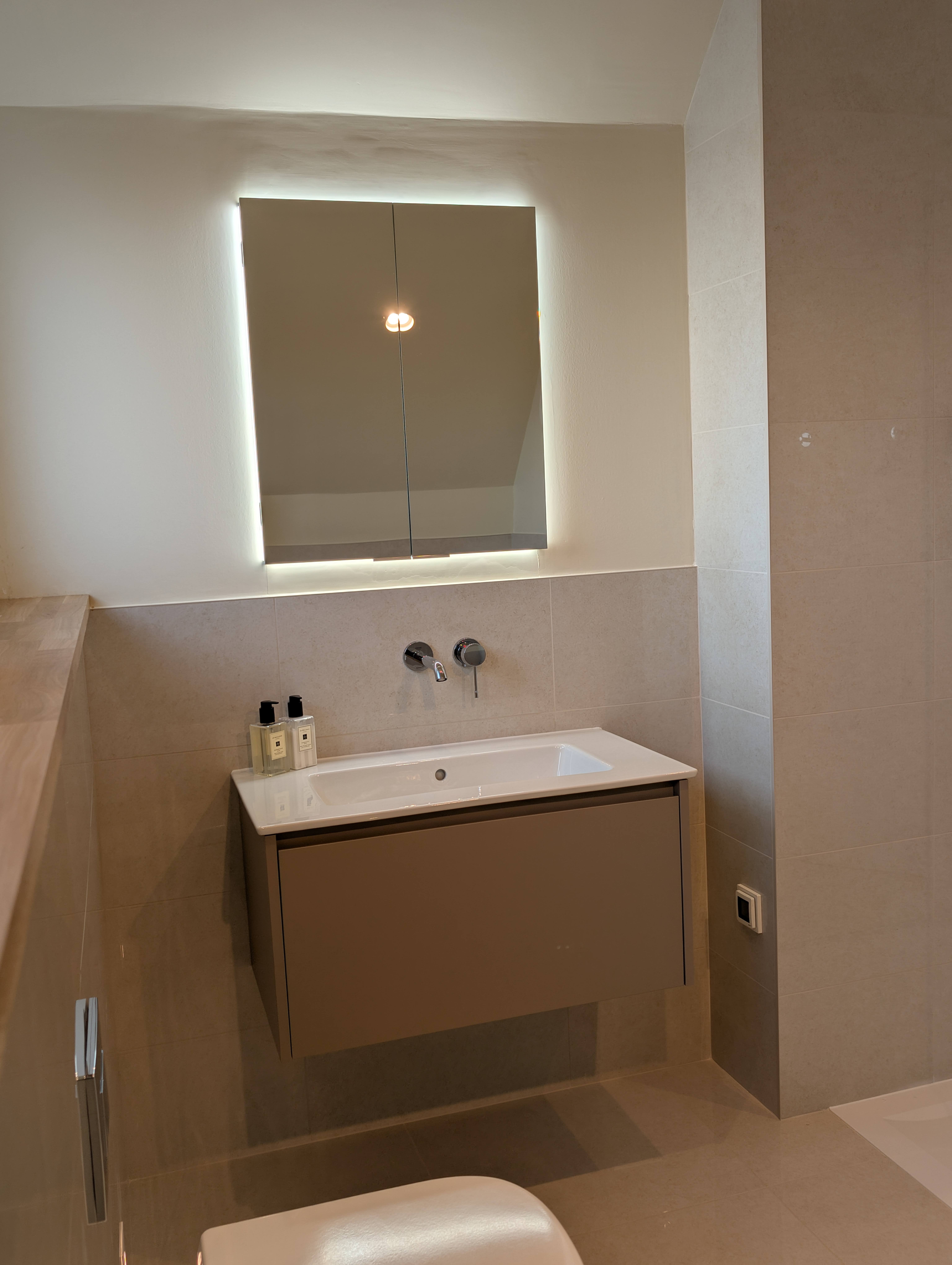 Wall-mounted basin below an illuminated mirrored cabinet